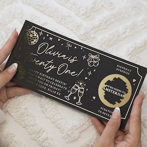 Könnte beinhalten: Eine schwarze, rechteckige Rubbelkarte für eine Geburtstagsüberraschung mit Goldfolienakzenten. Der Text lautet Olivia is Twenty One, Happy Birthday Bestie und We're Going to Amsterdam. Sie zeigt Illustrationen einer Discokugel, Kirschen und Champagnergläser.