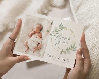 May include: A white thank you card with a green floral wreath and gold accents. The card features a photo of a baby sleeping on a white blanket. The text on the card reads "Thank you" and "Sofia Grace 12.02.2025 | 7LBS 9OZ".