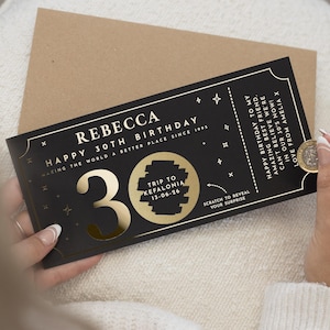 May include: A black and gold scratch card for a 30th birthday, with the name "Rebecca" and the text "Trip to Kefalonia." A coin is used to reveal the surprise. The card is on a white surface.