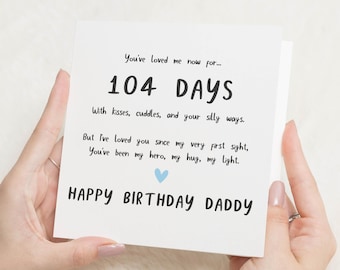 May include: A white greeting card with black text that reads "You've loved me now for... 104 DAYS" and "HAPPY BIRTHDAY DADDY." The card has a blue heart and is held by a person.