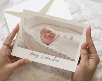 May include: A white card with a photo of a baby sleeping in a white basket. The card says "Baby Richardson" in cursive.