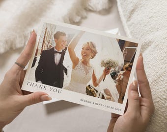 Peut inclure: Une carte de remerciement de mariage avec une photo d'une mariée et d'un marié. La mariée porte une robe blanche et le marié porte un costume noir. La carte dit "Merci" et "Georgie & Henry | 30.06.2025".