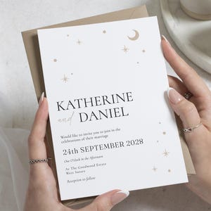 May include: A wedding invitation with the names KATHERINE and DANIEL in black and a script font. The invitation includes the date, time, and location of the wedding, with celestial design elements in gold.