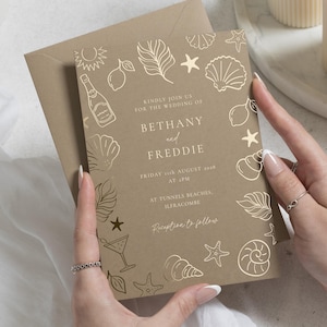 Può includere: Un invito di nozze color marrone chiaro con illustrazioni a linee in lamina d'oro raffiguranti conchiglie, stelle marine, limoni e una bottiglia di champagne. Il testo recita: Kindly join us for the wedding of Bethany and Freddie, Friday 11th August 2028 at 2pm, at Tunnels Beaches, Ilfracombe. Reception to follow.