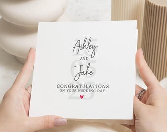 Op de afbeelding: Witte kaart met zwarte tekst die "Ashley en Jake Gefeliciteerd met jullie huwelijk" luidt, met een klein rood hartje.
