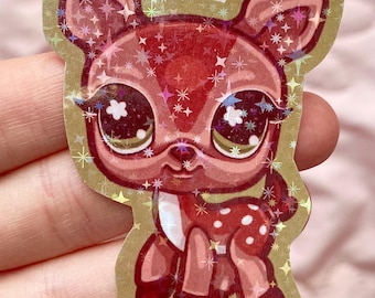 May include: A sparkly red deer sticker with large, glittery eyes and white polka dots. The sticker is on a brown background.