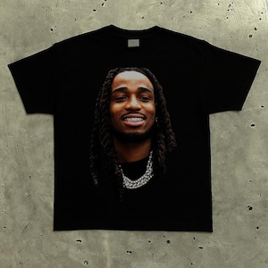Puede incluir: Camiseta negra con un retrato de un hombre con largas rastas, brackets y una cadena de diamantes. La imagen está centrada en la camiseta, mostrando los detalles faciales y las joyas sobre la tela oscura.