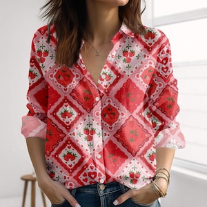 Könnte beinhalten: Rotes und weißes Hemd mit Knöpfen und Erdbeermuster. Das langärmlige Hemd hat ein sich wiederholendes Design aus Erdbeeren, Herzen und Rauten. Das Hemd hat einen Kragen und ist aus leichtem Stoff gefertigt.