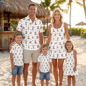 Könnte beinhalten: Eine Familie trägt passende weiße Kleidung mit einem sich wiederholenden Zeichentrickfiguren-Muster. Das Set besteht aus einem kurzärmeligen Hemd mit beiger Shorts, einem ärmellosen Kleid sowie zwei kurzärmeligen Hemden mit Jeans-Shorts.