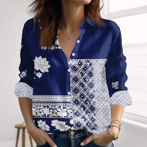 May include: Navy blue long-sleeved shirt with white floral and geometric patterns. The shirt has a V-neck and button fastenings. The cuffs and lower front panel feature a white floral border.