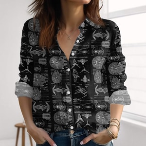 Può includere: Camicia nera abbottonata con un motivo ripetuto di progetti bianchi di varie astronavi. La camicia a maniche lunghe ha uno scollo a V e bottoni bianchi. I polsini sono arrotolati.
