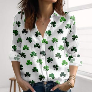 Puede incluir: Camisa blanca con estampado de tréboles verdes. Los tréboles tienen diferentes diseños, algunos lisos y otros con estampado de cuadros. La camisa de manga larga tiene cuello en V y se lleva con vaqueros azules. Tema del Día de San Patricio.