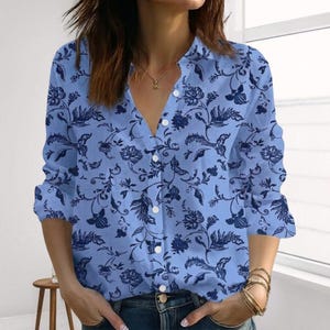 May include: A light blue button-down shirt with a floral pattern in a darker shade of blue. The long-sleeved shirt has a V-neck and is partially unbuttoned. The shirt is made of a lightweight fabric.
