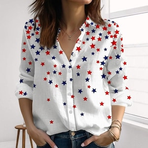 Könnte beinhalten: Weißes Button-Down-Hemd mit V-Ausschnitt, verziert mit einem Muster aus roten und blauen Sternen. Das langärmlige Hemd ist aus leichtem Stoff gefertigt und hat ein klassisches Knopfdesign, das sich für Freizeitkleidung eignet.