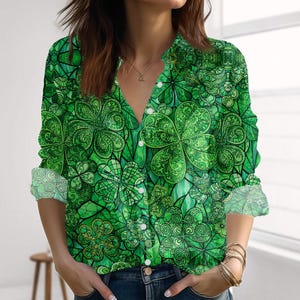 May include: Green long-sleeved shirt with a shamrock pattern. The shirt has a vibrant green colour scheme with detailed clover designs. The cuffs are rolled up, revealing a patterned interior. The shirt has white buttons.