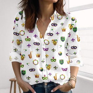 Peut inclure: Chemise blanche boutonnée ornée d'un motif répété de masques de Mardi Gras, de couronnes, de fleurs de lys et d'instruments de musique verts, violets et dorés. La chemise à manches longues a un col en V et est déboutonnée en haut.