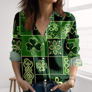 May include: Green and black button-down shirt with a St. Patrick's Day theme. The shirt features a repeating pattern of shamrocks and Celtic knot designs in shades of green and yellow. The long-sleeved shirt has a collared neckline and buttoned cuffs.