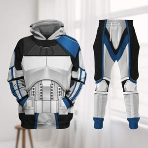 Könnte beinhalten: Ein passendes Hoodie- und Jogginghosen-Set. Der Hoodie ist weiß, schwarz und blau und soll an die Rüstung eines Sturmtrupplers erinnern. Die Jogginghose ist weiß mit schwarzen und blauen Akzenten, die das Design des Hoodies widerspiegeln.