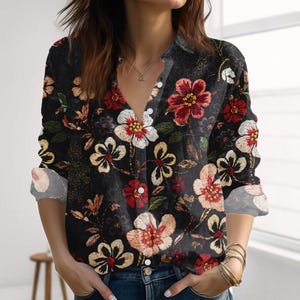 Könnte beinhalten: Schwarzes Button-Down-Shirt mit floralem Muster. Das langärmlige Hemd hat einen V-Ausschnitt und ist mit roten, weißen und gelben Blumen verziert. Die Manschetten sind hochgekrempelt und zeigen einen helleren Blumendruck.