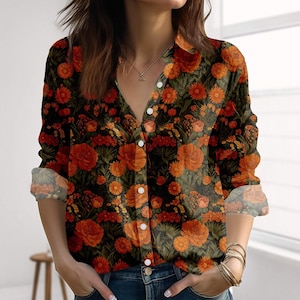 May include: A button-down shirt with a floral pattern in shades of orange, red, and yellow on a black background. The long-sleeved shirt has a collared neckline and white buttons. The sleeves are rolled up, revealing the floral pattern on the cuffs.