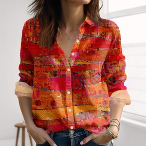 Könnte beinhalten: Ein langärmliges Hemd mit Knöpfen und einem lebendigen abstrakten Muster in Rot-, Orange- und Rosatönen. Das Hemd hat einen Kragen und weiße Knöpfe. Die Manschetten sind hochgekrempelt und zeigen einen helleren, gemusterten Stoff.