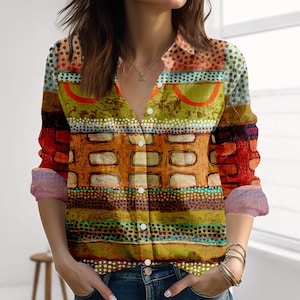 Könnte beinhalten: Ein Hemd mit Knöpfen und einem farbenfrohen, abstrakten Design. Das Hemd weist eine Mischung aus Mustern auf, darunter Streifen, Punkte und rechteckige Formen in Orange-, Grün-, Braun- und Blautönen. Die Ärmel sind hochgekrempelt und zeigen eine kontrastierende rosa und lila Manschette.