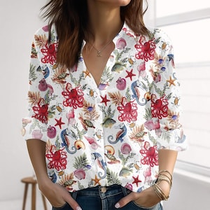 Könnte beinhalten: Weißes Button-Down-Shirt mit einem lebendigen Allover-Print mit roten Oktopussen, Seesternen, Muscheln, Seepferdchen und Fischen. Das langärmlige Hemd hat einen V-Ausschnitt und ist aus leichtem Stoff gefertigt.