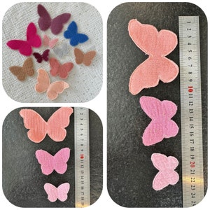 Könnte beinhalten: Sortiment an Filz-Schmetterlingsformen in verschiedenen Farben, darunter Rosa, Rot, Braun, Blau und Lila. Die Schmetterlinge sind auf einer weißen, strukturierten Oberfläche mit einem Lineal im Hintergrund angeordnet.