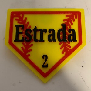 May include: A yellow and red baseball-shaped sign with the name "Estrada" and the number "2" printed in black.