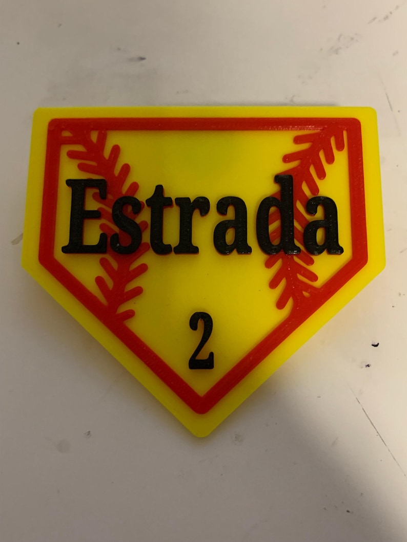 May include: A yellow and red baseball-shaped sign with the name "Estrada" and the number "2" printed in black.