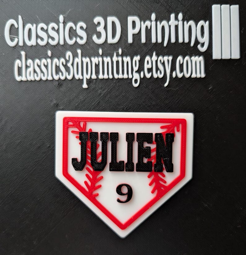 May include: A white baseball home plate with a red outline and red stitching. The name "JULIEN" is printed in black letters and the number "9" is printed in black below the name.