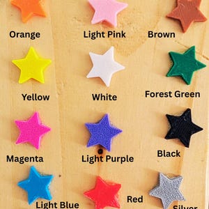 May include: Color options for a product, shown as a collection of 15 star-shaped plastic pieces in various colors, including royal purple, royal blue, navy, orange, light pink, brown, yellow, white, forest green, black, magenta, light purple, red, light blue, silver, gold, maroon, neon green, and teal.