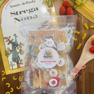 May include: A children's play set with a clear bag containing pasta shapes, wooden spoons, and a book titled "Strega Nona" by Tomie dePaola. The set includes a "Magic Pasta Pot" label and fresh tomatoes.