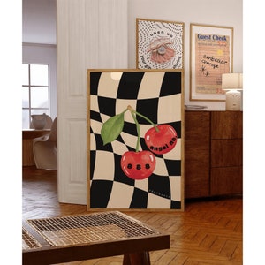 May include: A framed art print featuring a pair of red cherries with the text "angel no" and "888" on a black and beige checkered background. Additional framed prints are visible in the background, including one with a pearl and the words "open up".