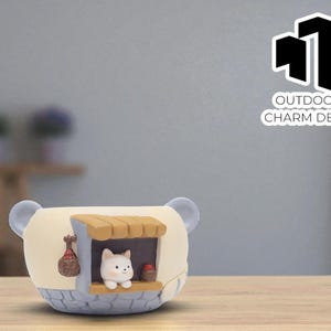 May include: A whimsical, cream-colored planter shaped like a bear with blue accents. It features a small, white cat figurine in a miniature house. The planter has a decorative bag and the text "OUTDOOR CHARM DECO".