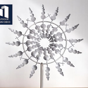 Könnte beinhalten: Ein silberner Metall-Windspinner für den Außenbereich mit kreisförmigem Design. Der Spinner weist eine Reihe von abgerundeten, kugelartigen Formen auf, die von einem zentralen Ring nach außen strahlen. Das Logo "OUTDOOR CHARM DECO" befindet sich in der oberen linken Ecke.