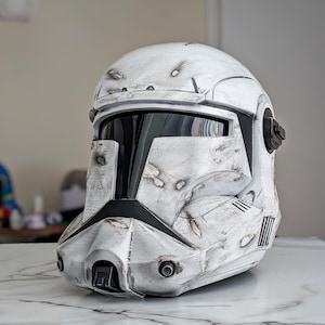 May include: A weathered white and gray helmet with black visor and accents. The helmet has a battle-worn appearance with visible wear and tear, including simulated blaster marks. The design is reminiscent of a science fiction or military aesthetic.