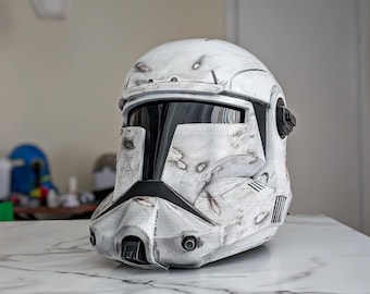 May include: A weathered white and gray helmet with black visor and accents. The helmet has a battle-worn appearance with visible wear and tear, including simulated blaster marks. The design is reminiscent of a science fiction or military aesthetic.