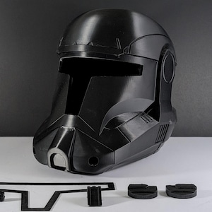 May include: A black helmet with a distinctive visor and angular design, reminiscent of a sci-fi aesthetic. The helmet is accompanied by several black components, suggesting a modular or customizable design. The overall appearance is sleek and futuristic.