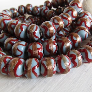 May include: A strand of blue and red glass beads with gold accents. The beads have a wavy pattern and are strung together on a wire.