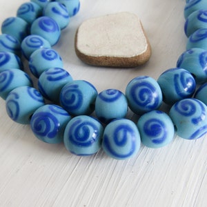 May include: A strand of blue and white ceramic beads with a swirl pattern. The beads are round and have a glossy finish.
