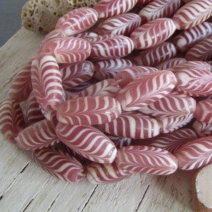 Op de afbeelding: Een streng roze en witte glazen kralen met een swirl-patroon. De kralen zijn ovaalvormig en hebben een glanzende afwerking.