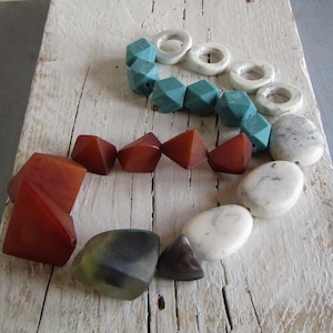 Può includere: Assortimento di perline colorate di varie forme. Include perline sfaccettate turchesi, perline bianche a forma di anello, perline geometriche marrone rossiccio e perline ovali bianche e grigie. Disposte su una superficie di legno invecchiato.