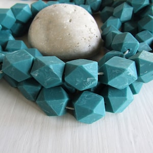 Può includere: Perle in silicone blu turchese a forma geometrica sfaccettata. Le perle sono infilate su un cordoncino bianco e sono disposte in un motivo circolare.