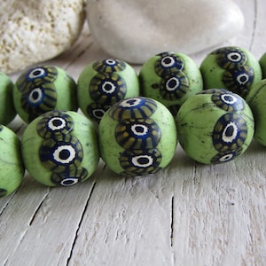 Peut inclure: Un collier de perles de verre vertes avec un motif géométrique blanc et bleu. Les perles sont rondes et ont une surface texturée.