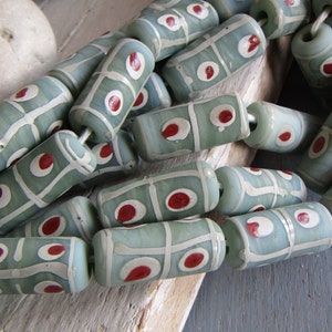 May include: A strand of green and white glass beads with red accents. The beads are cylindrical and have a geometric pattern.