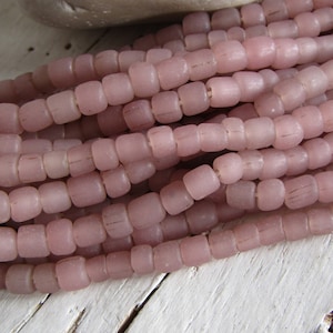Könnte beinhalten: Eine Strähne aus hellrosa Glasperlen, jede Perle ist quadratisch mit abgerundeten Kanten. Die Perlen sind undurchsichtig und haben eine leicht mattierte Oberfläche.