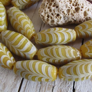 May include: A strand of yellow and white glass beads with a swirling pattern. The beads are oval shaped and have a glossy finish.