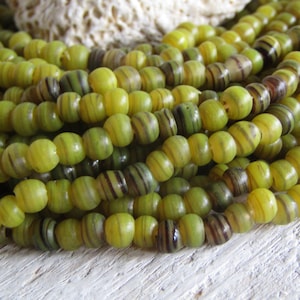 Può includere: Una collana di perline di vetro verde e giallo con un motivo a strisce. Le perline sono rotonde e hanno una finitura lucida.