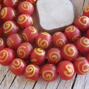 Op de afbeelding: Een streng rode kralen met gele swirl-ontwerpen. De kralen zijn rond en glad.